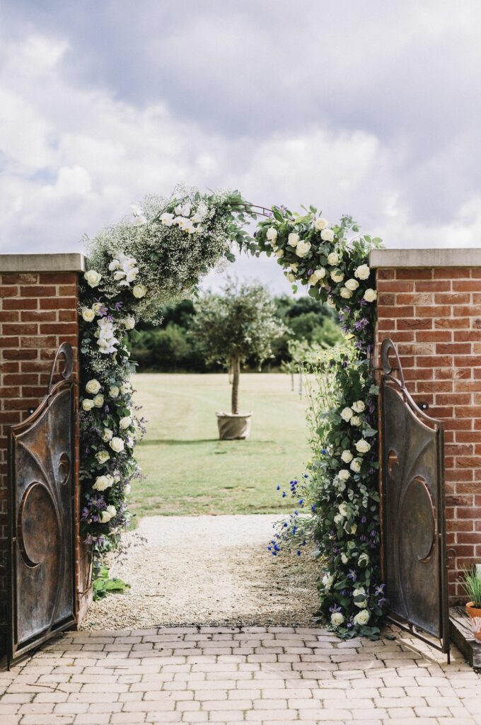 A door in a wall, and a white rose arch in a garden, with a view to a sundial.